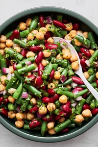 3 bean salad in a serving bowl with a serving spoon made with green beans, kidney beans, garbanzo beans, red onion & parsley