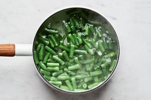 fresh green beans cut in to 1-inch pieces being blanched in a pot of boiling water