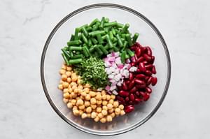 blanched green beans, kidney beans, garbanzo beans, chopped red onion and chopped parsley in a glass bowl
