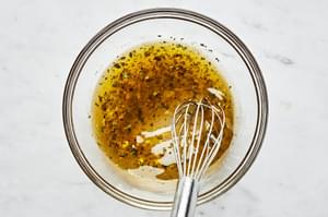 dressing being whisked in a bowl made with garlic, vinegar, sugar, basil, salt, pepper & olive oil