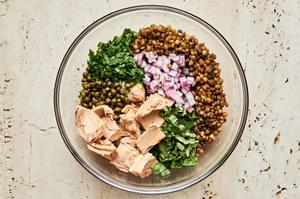 cooked lentils, tuna, red onion, capers, basil & parsley in a glass bowl to make tuna lentil salad