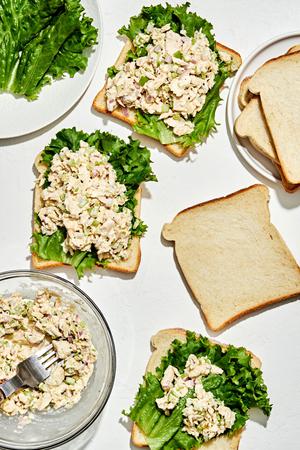 slices of bread on a counter being topped with lettuce and homemade tuna salad