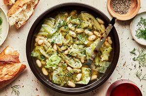 a bowl White Bean Soup with Dill and Cabbage being served with crusty bread