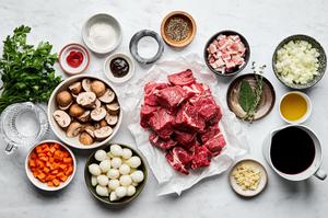 chuck roast, bacon, spices, tomato paste, flour, red wine, bouillon, olive oil, onion, carrots, and mushrooms in bowls