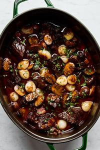 a pot of beef bourguignon made with mushrooms, pear onions, carrots, onion, tomato paste, red wine, and spices