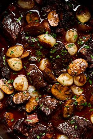 a pot of beef bourguignon made with mushrooms, pear onions, carrots, onion, tomato paste, red wine, and spices