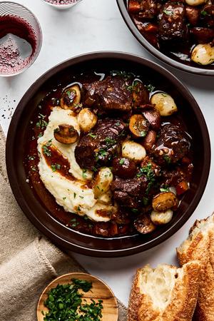 homemade beef bourguignon with mushrooms and pearl onions being served on top of classic mashed potatoes