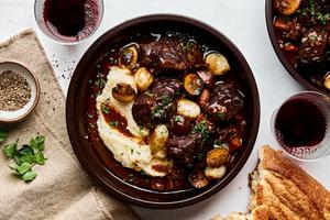 homemade beef bourguignon with mushrooms and pearl onions being served on top of classic mashed potatoes