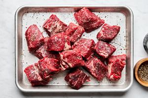 cubed chuck roast being seasoned with salt and pepper