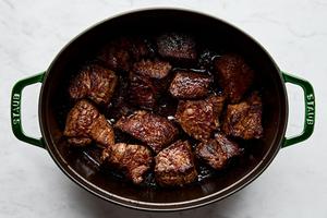 chuck roast pieces seasoned with salt and pepper being browned in bacon fat in a dutch oven