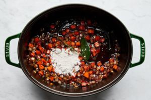 onion, carrot, garlic, tomato paste, bay leaf, thyme and flour being cooked in bacon fat in a dutch oven
