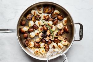 mushrooms and pearl onions being coked in a skillet with olive oil and salt