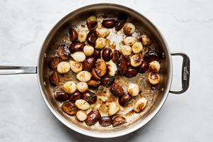 mushrooms and pearl onions being cooked in a skillet with olive oil and salt