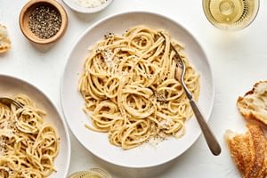 2 bowls of cacio e pepe topped with Parmesan and pepper being served with bread