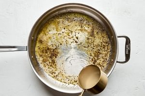 reserved pasta water being poured into a skillet with olive oil, butter and pepper