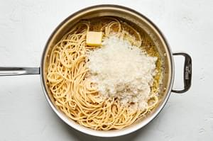 cooked bucatini, Parmesan and Romano being added to a skillet with olive oil, butter, pepper and reserved pasta water