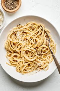 a bowl of cacio e pepe made with bucatini, extra-virgin olive oil, butter, pepper, Parmesan and Romano topped with pepper