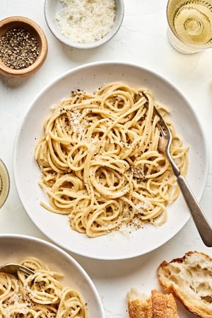 2 bowls of cacio e pepe topped with Parmesan and pepper being served with bread
