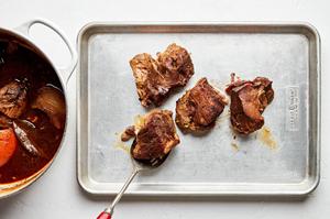 cooked carnitas being placed on a baking sheet to broil until crispy