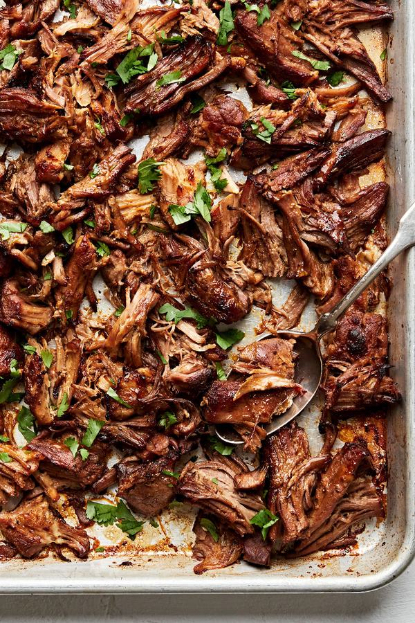 homemade carnitas on a baking sheet seasoned with bay leaves, oregano, chili powder, salt, cumin, pepper & cayenne