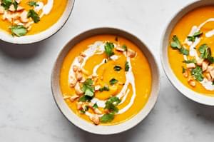 a bowl of carrot ginger soup drizzled with coconut milk and topped with cilantro and macadamia nuts