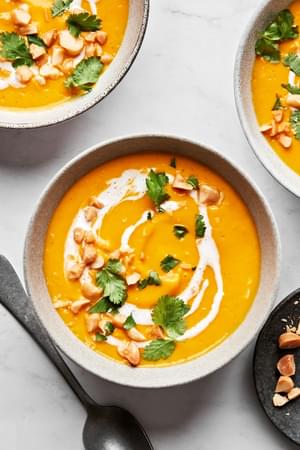 a bowl of carrot ginger soup drizzled with coconut milk and topped with cilantro and macadamia nuts