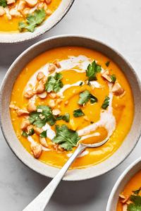 a bowl of carrot ginger soup drizzled with coconut milk and topped with cilantro and macadamia nuts