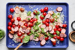 cauliflower rice, smoked sausage, tomatoes, pesto, salt & pepper being tossed together on a sheet pan