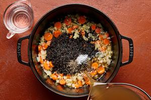 garlic and ginger being added to a pot with olive oil, onion and carrots