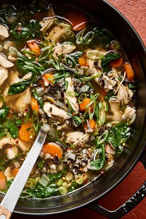 a ladle in a pot of chicken and wild rice soup made with carrots, garlic, ginger, onion, and spinach