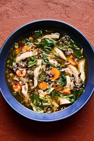 a bowl of chicken and wild rice soup made with carrots, spinach, garlic, ginger, spinach & green onions