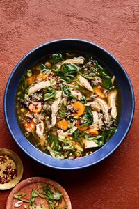 a bowl of chicken and wild rice soup made with carrots, spinach, garlic, ginger, spinach & green onions