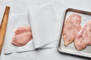 chicken breasts being pounded between parchment paper then seasoned with salt and pepper
