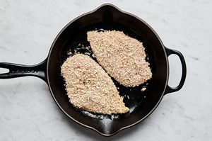 chicken breasts seasoned with salt and pepper dipped in egg and coated with panko and italian seasoning cooking in a skillet