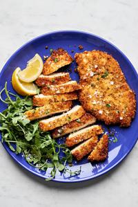 homemade chicken milanese sliced on a plate, sprinkled with flaky salt and served with lemon wedges
