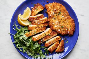 homemade chicken milanese sliced on a plate, sprinkled with flaky salt and served with lemon wedges