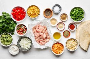 chicken, bell pepper, onion, corn, spices, cilantro, cheese, flour tortillas, guacamole, salsa and sour cream in prep bowls