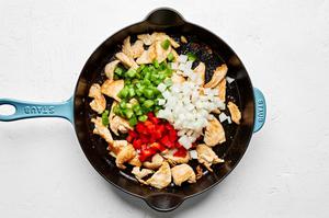 bell peppers and onions being added to a skillet with browned chicken