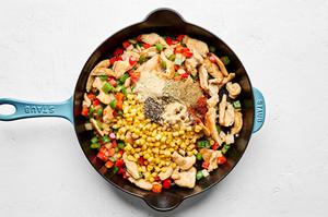 corn and spices being added to a skillet with bell peppers, onions and chicken
