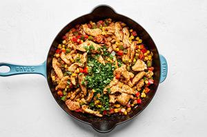 cilantro added to a skillet with corn, spices, bell peppers, onions and chicken