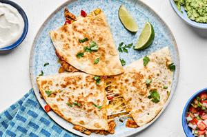 a sliced chicken quesadilla on a plate surrounded by sour cream, guacamole and pico de gallo for serving
