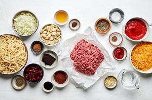 ground beef, stock, onion, garlic, tomatoes, Worcestershire, spices, chocolate, vinegar, cheese and spaghetti in prep bowls