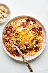 a bowl of Cincinnati chili served on spaghetti noodles topped with shredded cheese, kidney beans and oyster crackers