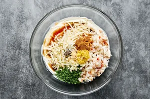 ingredients to make hot crab dip being stirred in a bowl including cream cheese, mayo, sour cream, spices, hot sauce & cheese