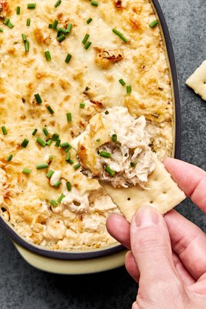 a cracker being dipped in crab dip made with cream cheese, mayo, sour cream, spices, white cheddar cheese and mozzarella