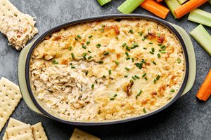 hot crab dip in a baking dish made with cream cheese, mayo, sour cream and cheese served with crackers and raw vegetables