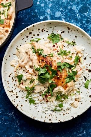creamy coconut lime chicken in a skillet topped with cilantro, green onions and red pepper flakes served on top of rice