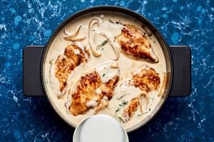 browned chicken being added back to a skillet of creamy coconut lime sauce