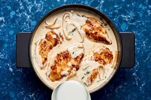 browned chicken being added back to a skillet of creamy coconut lime sauce