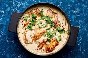 creamy coconut lime chicken in a skillet topped with cilantro, green onions and red pepper flakes